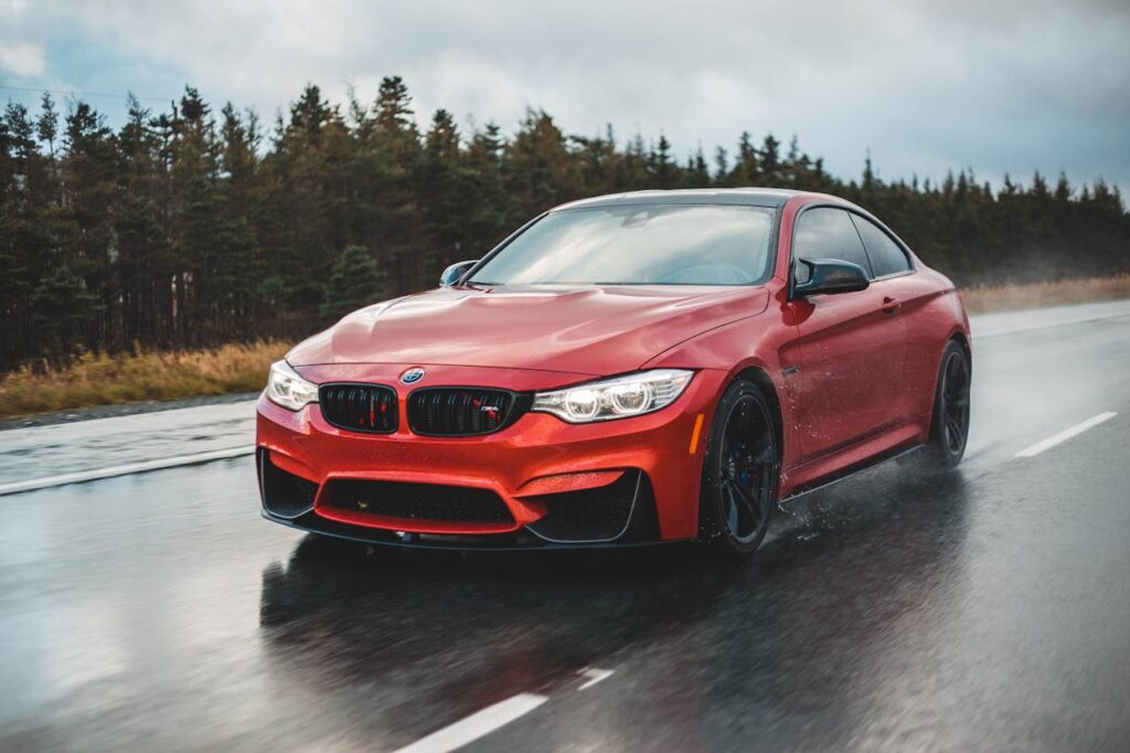 A sleek red sports car driving fast on a wet road surrounded by forests.