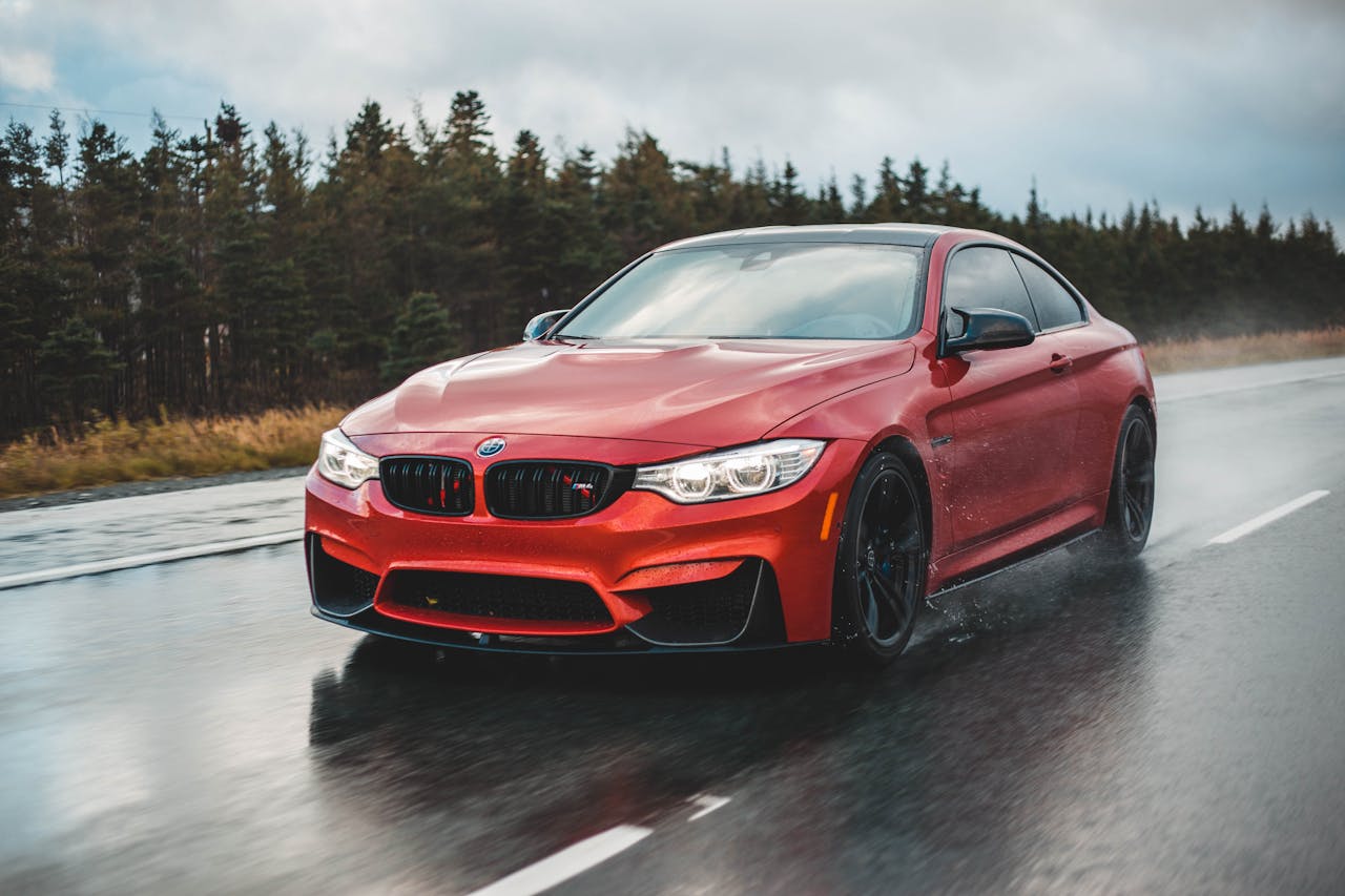 A sleek red sports car driving fast on a wet road surrounded by forests.